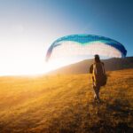 Paraglider letí vysoko nad krajinou s oblakmi v pozadí